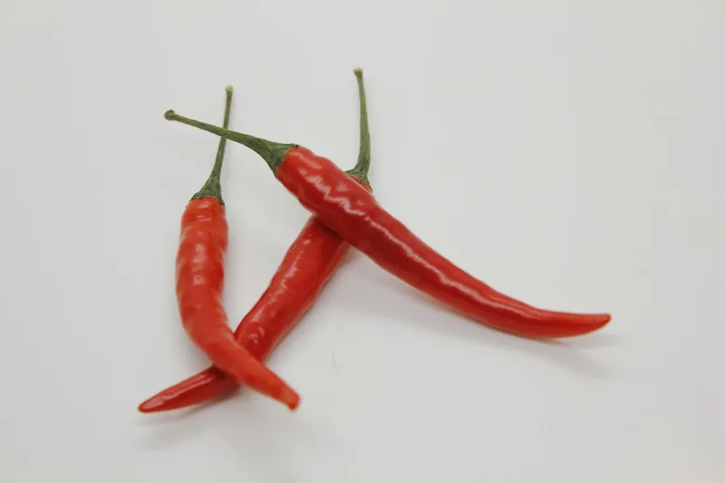 Hot peppers, also known as chili peppers, are fruits from the Capsicum genus, renowned for their fiery flavor, heat, and distinctive taste. These peppers contain capsaicin, a compound that causes the sensation of heat, and varies in concentration, determining the pepper's spiciness. Hot peppers come in a variety of shapes, sizes, and colors, ranging from small, slender varieties like bird's eye chilies to larger ones like jalapeรฑos and habaneros, as well as the extremely hot Carolina Reaper and ghost pepper.